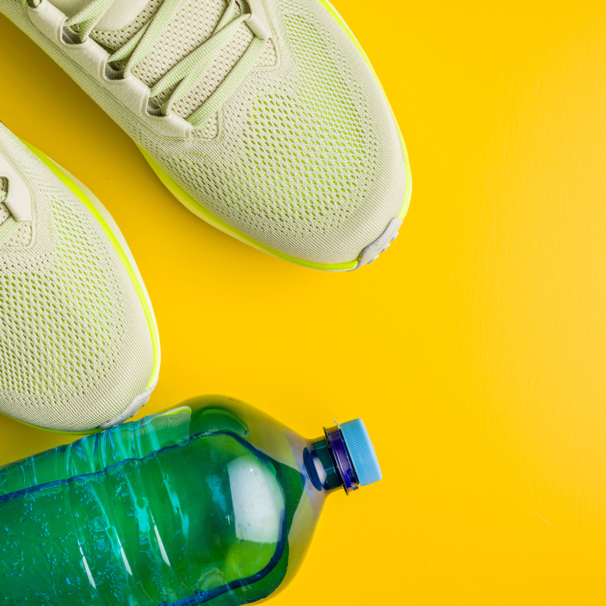 Turnschuhe und eine Trinkflasche vor gelbem Hintergrund